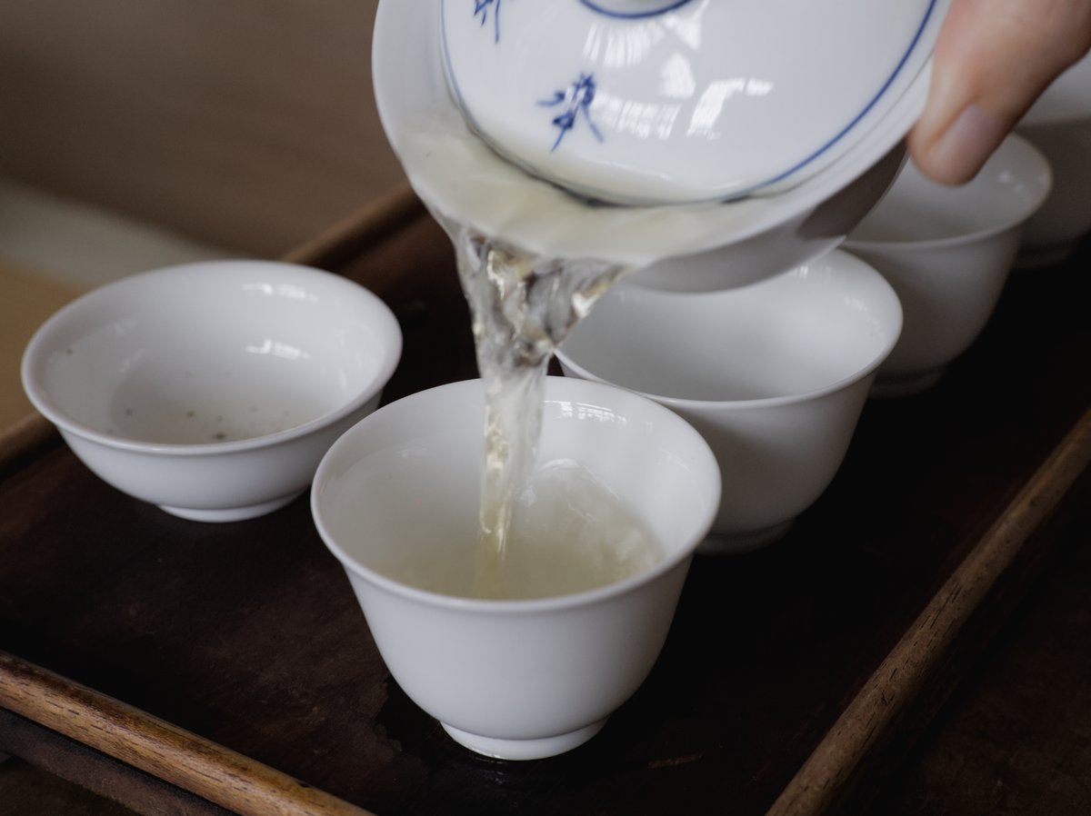 pouring naturally farmed oolong tea from gaiwan into porcelain cups