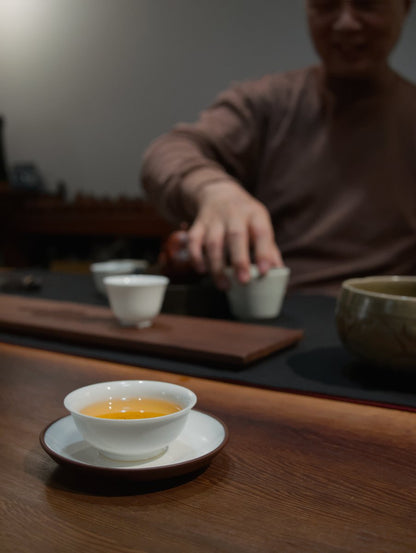 teacher Lai sitting behind dark wooden table brewing charcoal roasted oolong tea