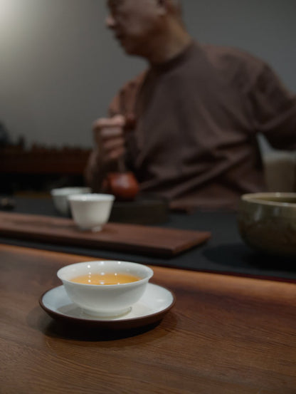 teacher Lai sitting behind a dark wooden table brewing his charcoal roasted oolong tea