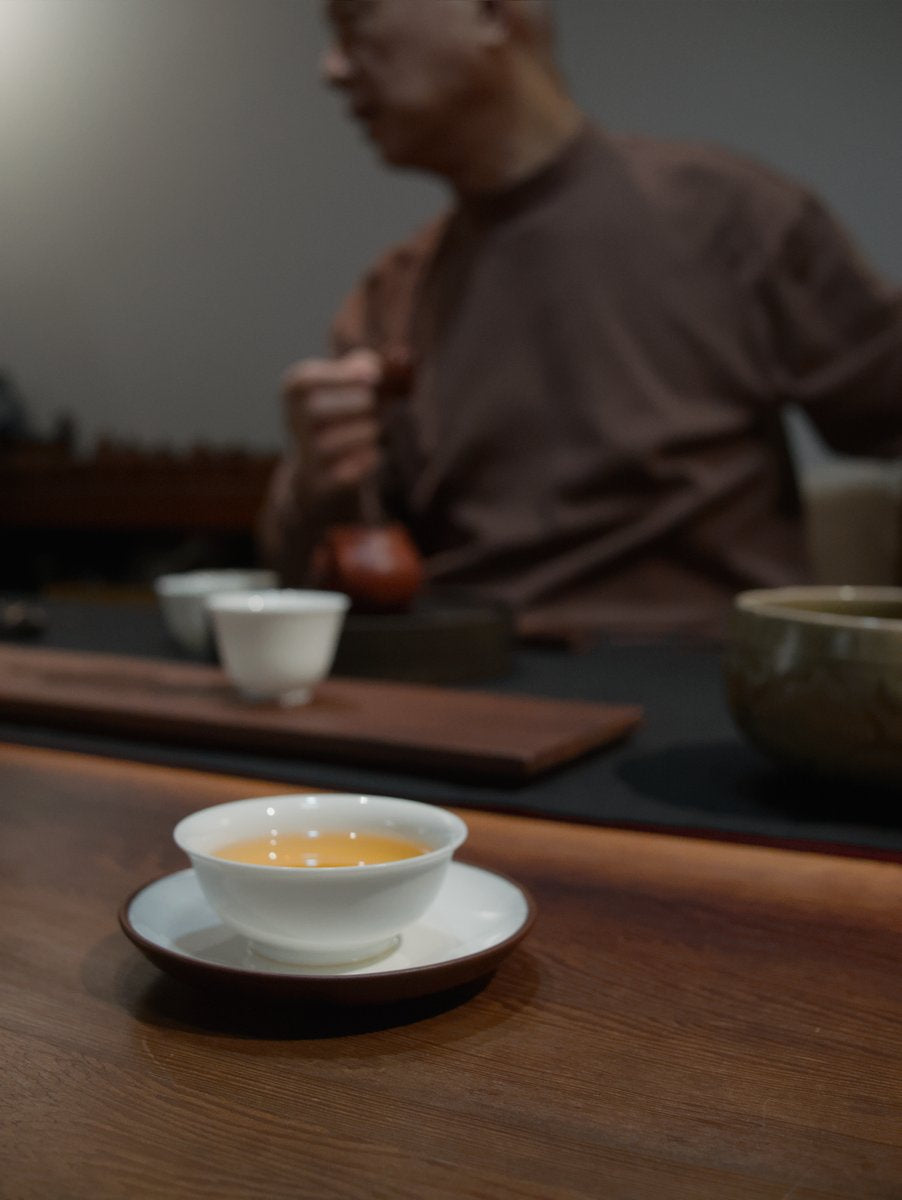 teacher Lai sitting behind dark wooden table brewing charcoal roasted oolong tea