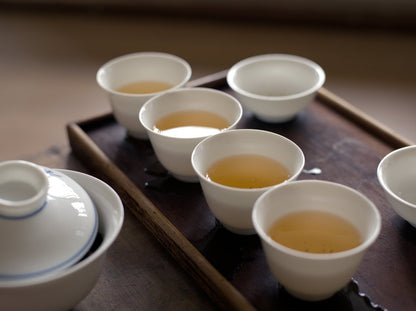 white porcelain cups filled with naturally farmed Tieguanyin oolong tea on a dark wooden board